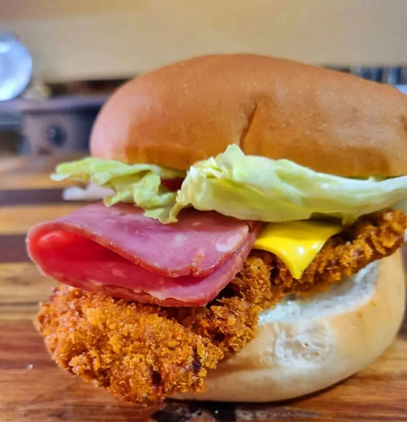 برگر فیله مرغ سوخاری ترد کافه و رستوران تراس لانژ، با پنیر چدار، کاهو تازه و کالباس دودی. یک وعده غذایی لذیذ و پرطرفدار.