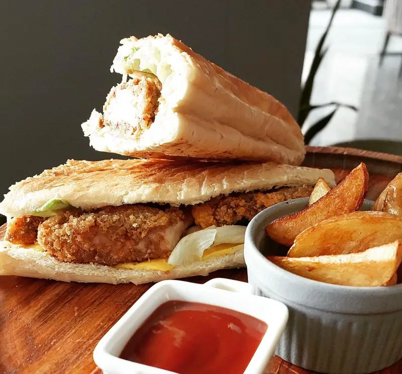 ساندویچ‌های خوشمزه کافه و رستوران تراس لانژ شامل مرغ سوخاری ترد، پنیر و کاهو، همراه با وج سیب‌زمینی و سس کچاپ.