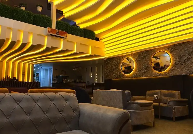 نمای داخلی شیک کافه برلین با نورپردازی مدرن و گرم زرد رنگ، سقف‌های موج‌دار و خطی، مبلمان راحت و آینه‌های دکوراتیو.