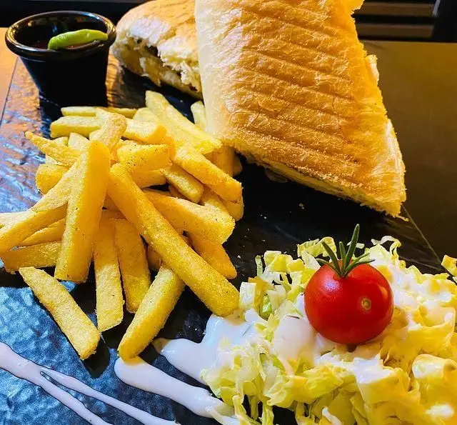 تصویر ساندویچ پانینی گریل شده و ترد کافه برلین، سرو شده با سیب زمینی سرخ کرده، سالاد تازه و سس مخصوص. انتخابی عالی برای ناهار و شام.