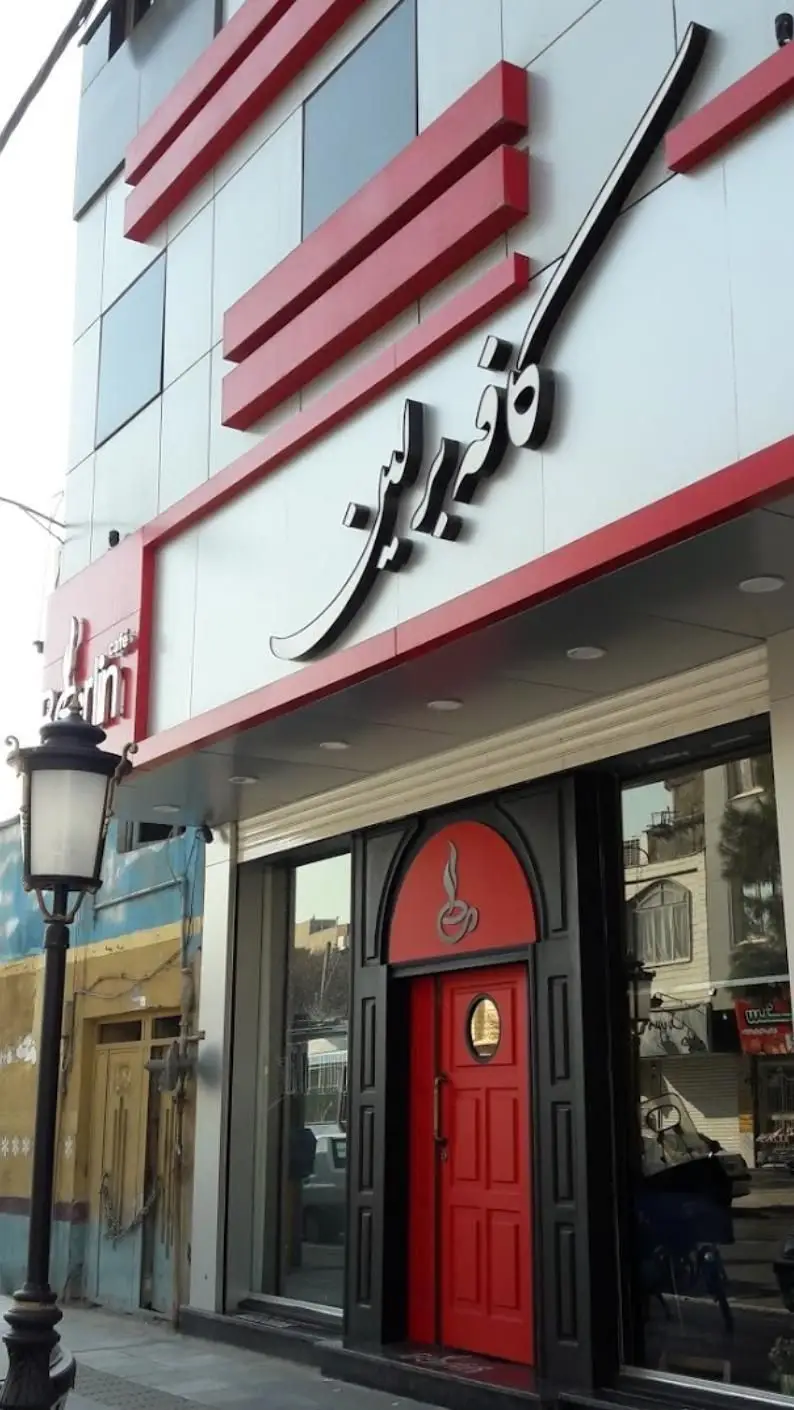 نمای بیرونی شیک کافه برلین با تابلوی بزرگ فارسی، درب ورودی قرمز مدرن با لوگوی فنجان قهوه، طراحی جذاب برای کافی شاپ.