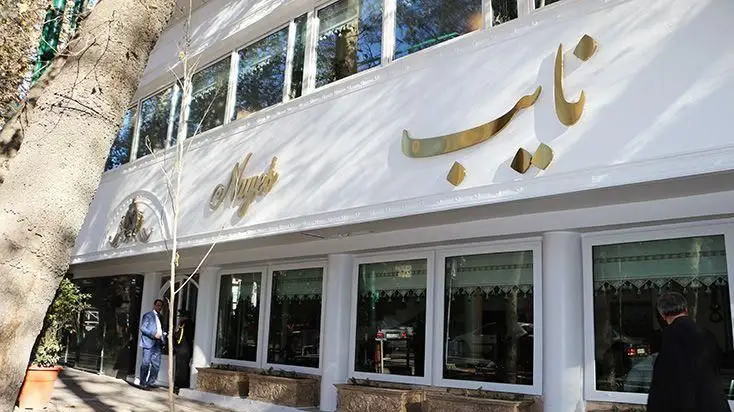 نمای بیرونی رستوران نایب باغ فردوس تهران، ساختمانی سفید با تابلو طلایی نایب و پنجره‌های بزرگ، آماده پذیرایی از میهمانان.