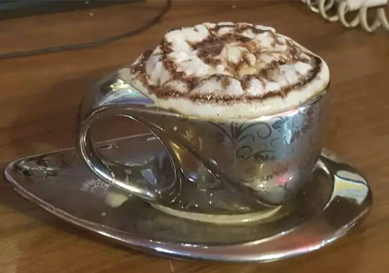 کاپوچینو لذیذ در ظروف نفیس نقره‌ای کافه قلیان و سفره خانه سنتی کولاک، تجربه‌ای دلنشین از نوشیدنی‌های گرم در محیطی آرام و زیبا.