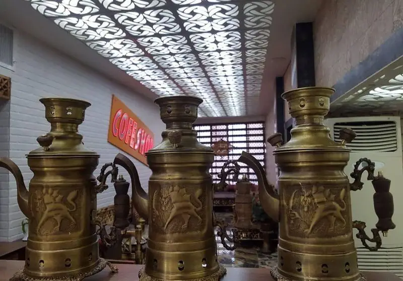 سه سماور برنزی سنتی با نقوش زیبا، در دکوراسیون خاص کافه قلیان و سفره خانه سنتی کولاک، زیر سقف طرح دار و نورپردازی نئون.