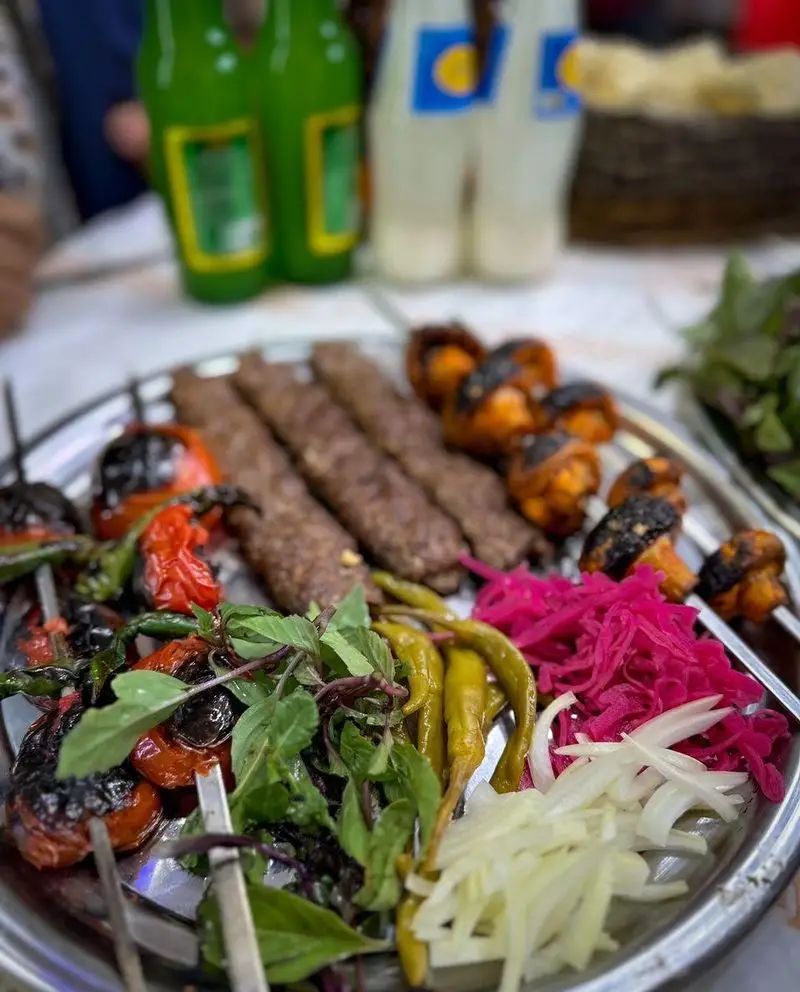 سینی کباب کوبیده و سبزیجات کبابی شامل قارچ، گوجه و فلفل همراه با سبزی تازه، پیاز، کلم قرمز در کافه قلیان و سفره خانه سنتی کولاک.