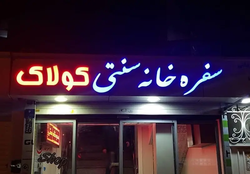 سفره خانه سنتی و کافه قلیان کولاک با تابلو نئون در شب، ارائه دهنده غذاهای سنتی و سرو قلیان برای مشتریان.