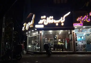 تصویر شب از نمای بیرونی کباب سرای تنور با تابلوی نئونی روشن و دکوراسیون داخلی آشکار، آماده پذیرایی از مشتریان.