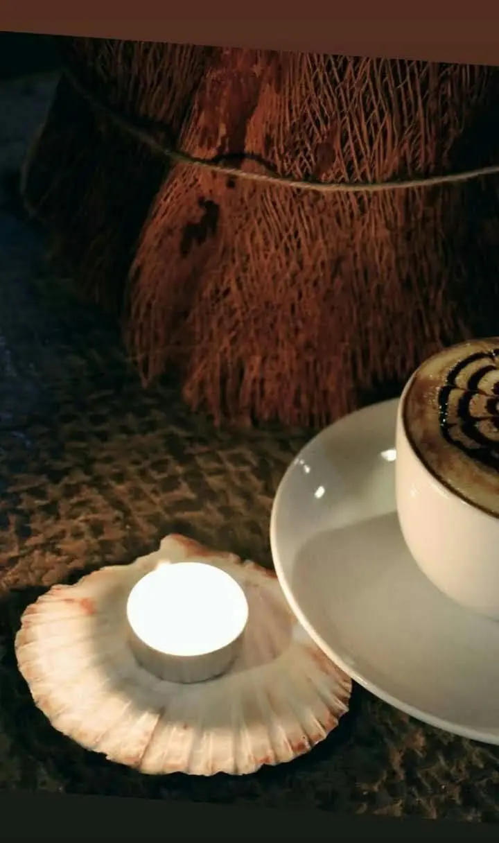 تجربه لذت‌بخش قهوه لاته هنری با طرح شکلاتی و نور گرم شمع در صدف، فضایی دنج و آرامش‌بخش در کافه سبز گمرون را به تصویر می‌کشد.