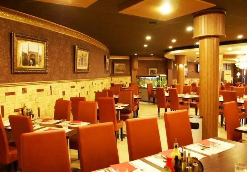 فضای داخلی شیک رستوران نمونه تهران با میز و صندلی‌های نارنجی، آکواریوم زیبا، نورپردازی گرم و محیطی دلنشین برای میهمانان.