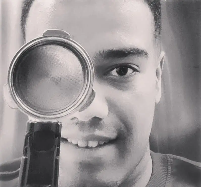 پرتره‌ای جذاب و سیاه و سفید از لبخند دلنشین یکی از کارکنان برگر دلشاد، با ابزار قهوه، بازتابی از کیفیت و رضایت مشتری