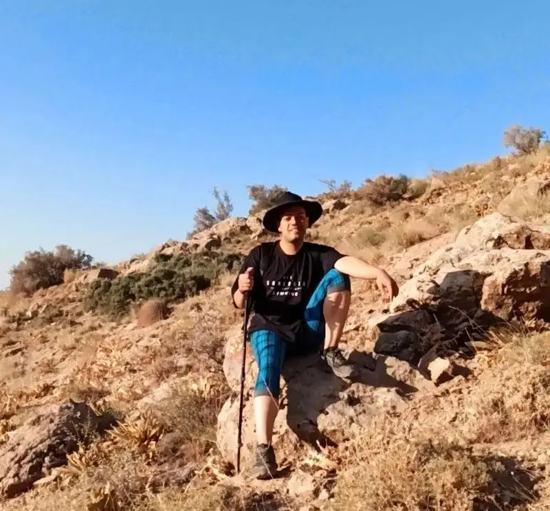 کوهنوردی با کلاه و عصا در شیب کوهستان صخره‌ای، در حال استراحت پس از یک صعود. بهترین جایزه: یک برگر دلشاد خوشمزه.