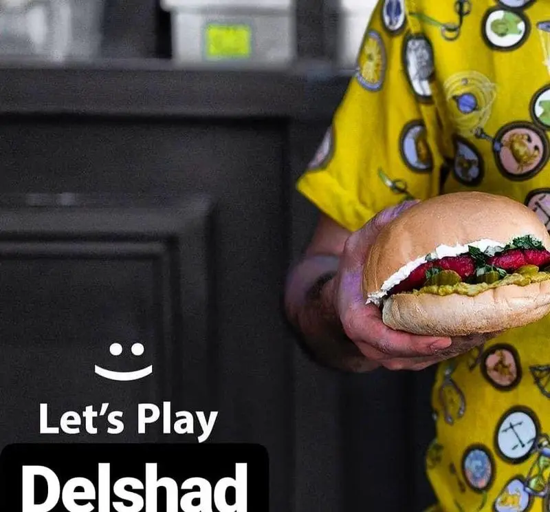 برگر دلشاد: یک همبرگر خوشمزه و لذیذ با نان تازه و مواد باکیفیت در دست یک شخص، آماده سرو در رستوران فست فود دلشاد.