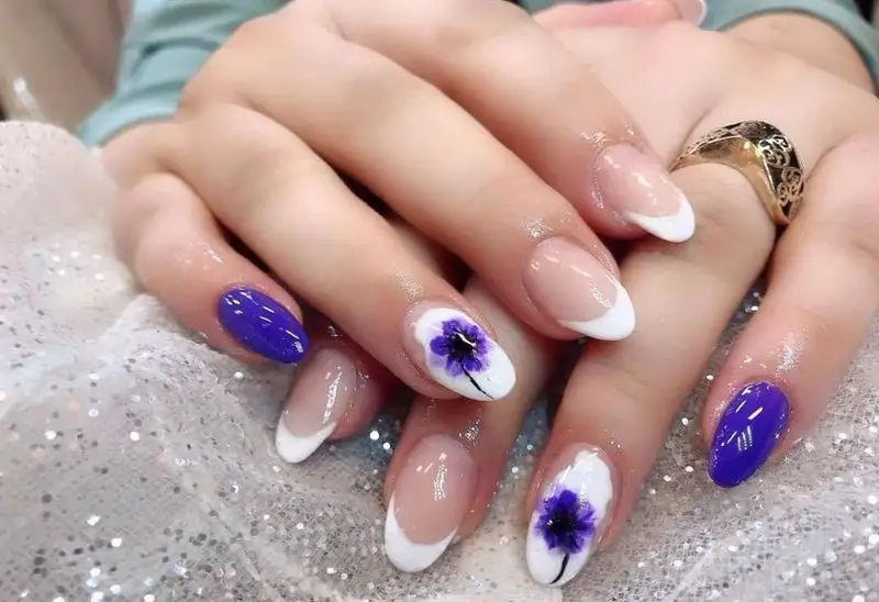 طراحی ناخن شیک و مجلسی با لاک بنفش و طرح گلهای مینیاتوری زیبا به همراه فرنچ ناخن کلاسیک روی دست زنانه با انگشتر طلا