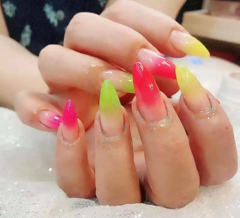 مدل طراحی ناخن آمبره با رنگهای شاد نئونی صورتی، زرد و سبز به همراه اکلیل نقرهای در پایه ناخنهای بلند و نوک تیز زنانه