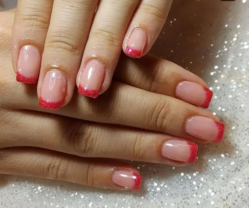 طراحی ناخن فرنچ شیک با پایه صورتی طبیعی و لبههای اکلیلی قرمز براق و درخشان روی ناخنهای مربعی و سوهانکشیده زنانه
