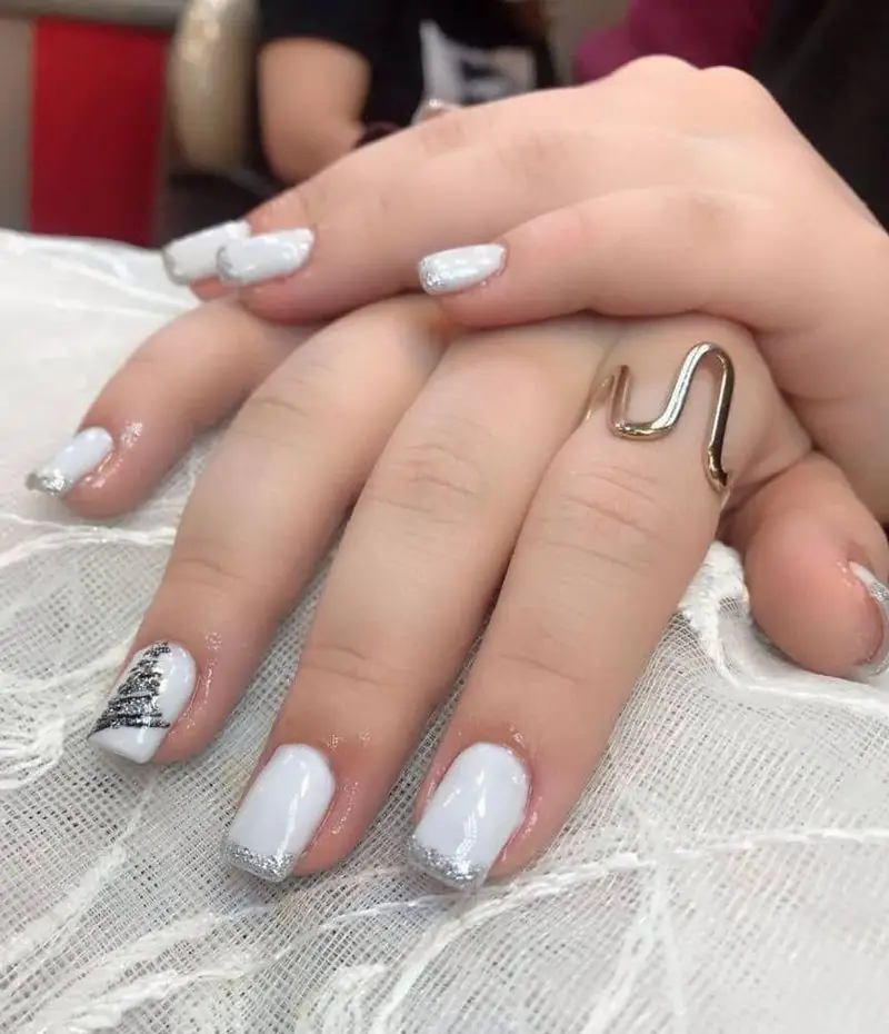 تصویر کاشت ناخن با لاک سفید و فرنچ نقرهای براق به همراه طرح درخت کریسمس روی ناخن انگشت حلقه و انگشتر فلزی مارپیچ