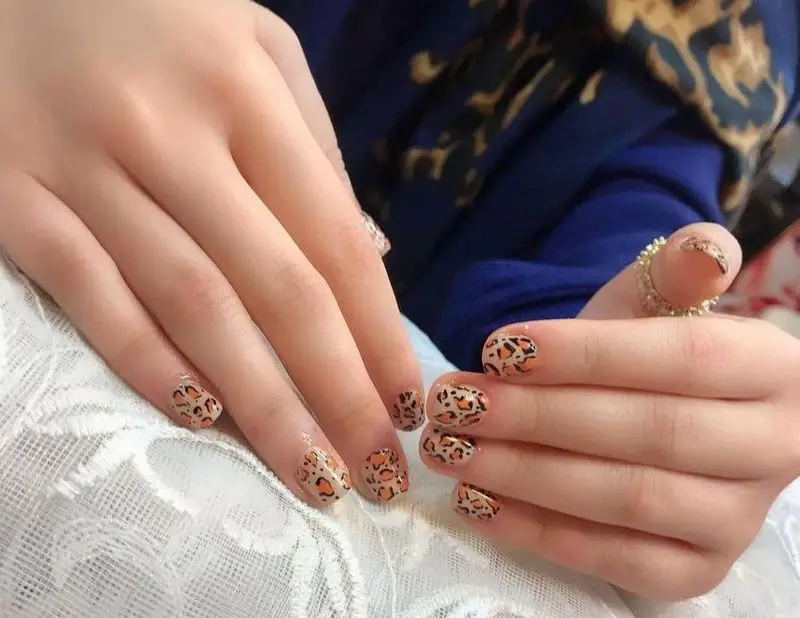 طراحی ناخن پلنگی با لاک نارنجی و قهوهای روی پایه کرم نود، نمونه کار کاشت و دیزاین ناخن در سالن خدمات تخصصی ناخن حدیث