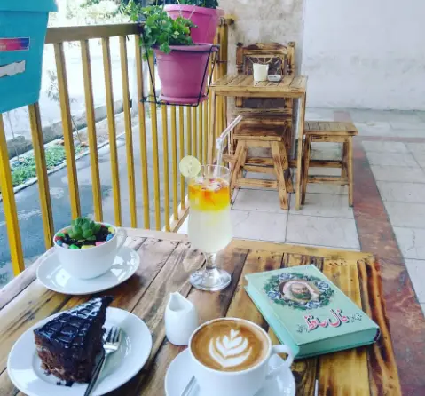 تجربه یک عصر دلنشین در کافه اوج: لذت قهوه لاته، کیک شکلاتی و نوشیدنی‌های خاص در فضای بالکن با میز چوبی.