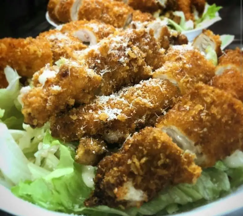 مرغ سوخاری طلایی و برش‌خورده رستوران ایتالیایی مازتی با سس مخصوص و پنیر پارمزان روی کاهو، یک غذای خوشمزه و جذاب.