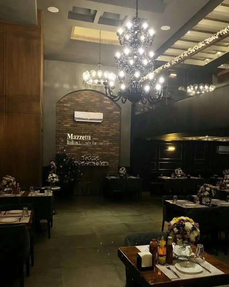 تصویری از محیط داخلی رستوران ایتالیایی مازتی، با دکوراسیون لوکس و مجلل، لوسترهای درخشان و میزهای چیده شده برای میزبانی خاص.