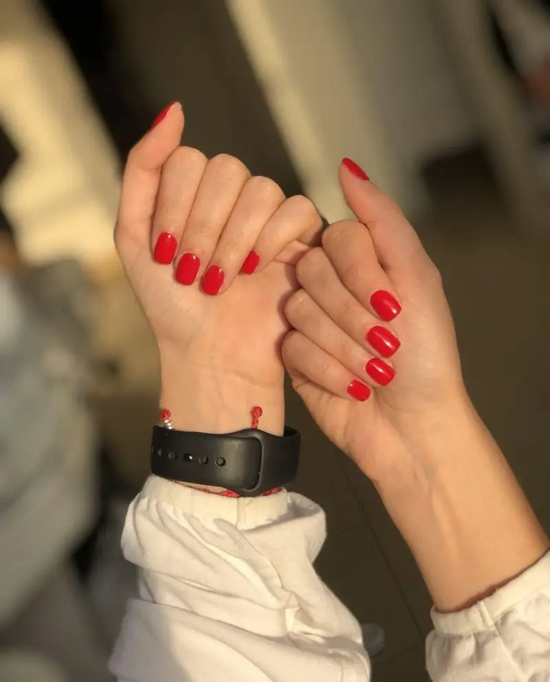 خدمات تخصصی کاشت و ژلیش ناخنهای کوتاه و مربعی با لاک قرمز کلاسیک و درخشان روی دستهای مشتری در سالن زیبایی ماه بیوتی