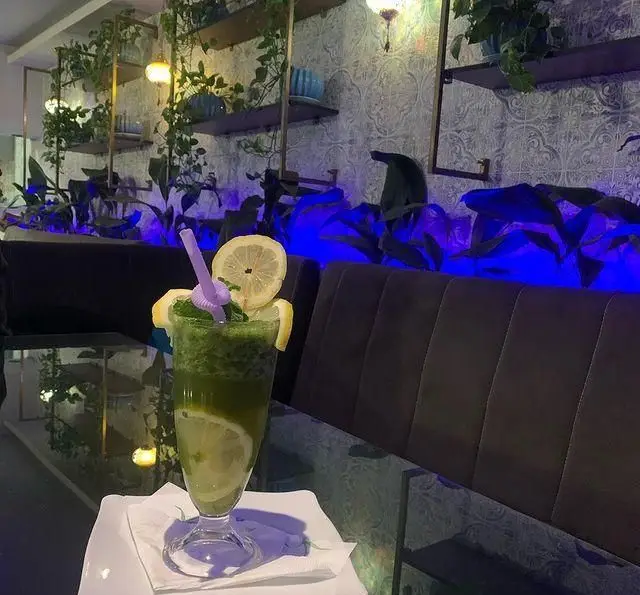 فضای داخلی رستوران و کافه الخلیفه با دکوراسیون شیک، نورپردازی آبی جذاب، گیاهان دیواری و نوشیدنی لیمو نعنای خنک.