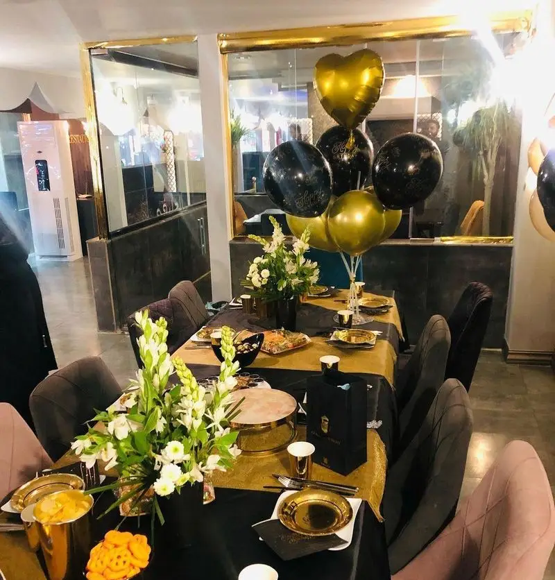 فضای داخلی لوکس و میزآرایی شیک رستوران و کافه الخلیفه برای جشن تولد و مهمانی‌های خاص، با بادکنک‌های طلایی مشکی و گل‌آرایی زیبا.