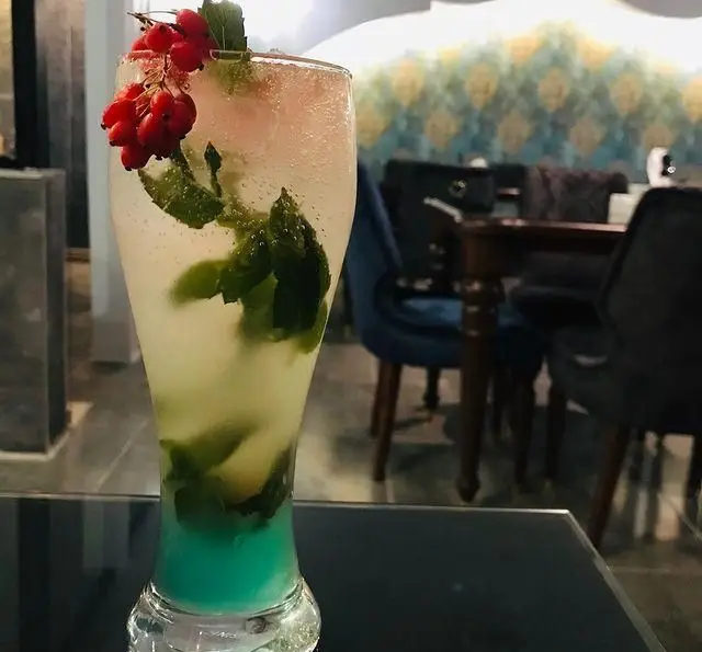 نوشیدنی موهیتو خنک و رنگارنگ با برگ‌های نعناع و تزیین توت قرمز، تجربه‌ای تازه از منوی ویژه رستوران و کافه الخلیفه.