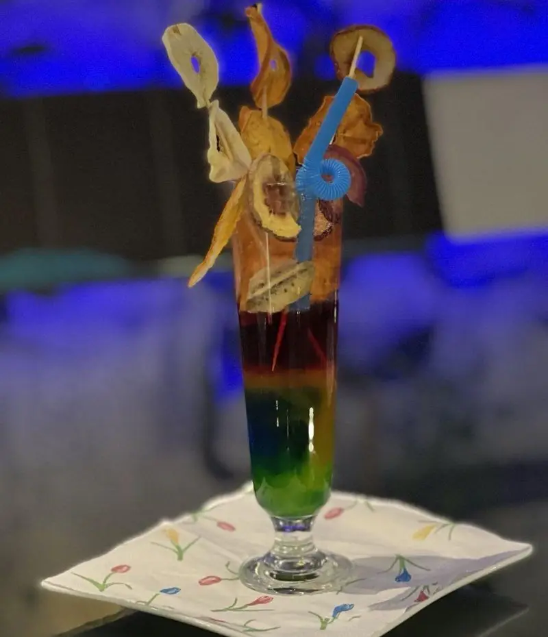 کوکتل چندلایه رنگین‌کمان با میوه‌های خشک تزئینی و نی فانتزی، نوشیدنی خاص کافه و رستوران الخلیفه برای تجربه‌ای متفاوت.