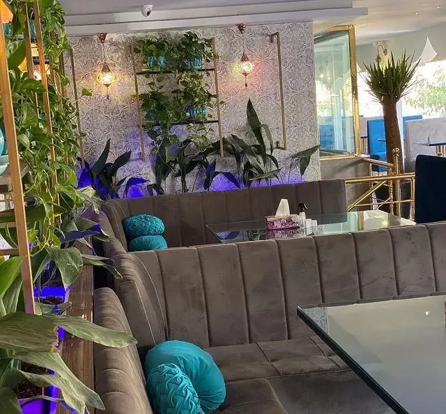 فضای داخلی آرامش‌بخش رستوران و کافه الخلیفه با مبلمان مخملی قهوه‌ای، گیاهان سبز فراوان، میزهای شیشه‌ای و نورپردازی زیبا.