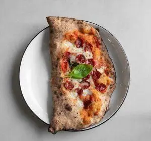 نیم پیتزا پپرونی یا کالزونه تنوری خوشمزه رستوران فرسکو با پنیر موزارلا، سس گوجه و ریحان تازه روی بشقاب سفید.