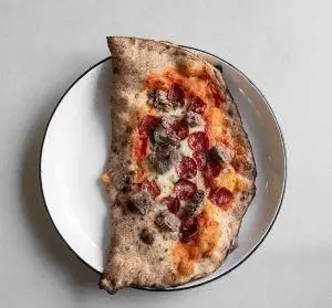 پیتزا تاشده یا کالزونه گوشت و پپرونی رستوران فرسکو با خمیر تنوری و پنیر فراوان روی بشقاب سفید، انتخابی خوشمزه برای غذای ایتالیایی.