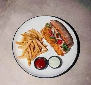 ساندویچ مرغ شنیتسل لذیذ با نان باگت، سیب‌زمینی سرخ‌کرده و سس کچاپ و مایونز. لذت طعم در رستوران فرسکو.