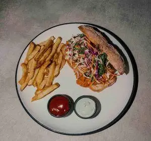 ساندویچ مرغ یا گوشت کشیده شده با سالاد کلم و سبزیجات تازه، به همراه سیب زمینی سرخ کرده و سس در رستوران فرسکو. غذایی لذیذ برای تجربه در فرسکو.