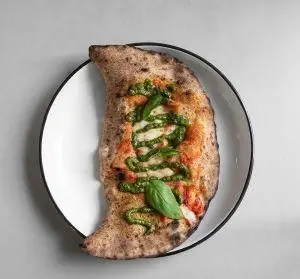 کالزونه تنوری رستوران فرسکو با خمیر دست‌ساز، سس پستو سبز، پنیر موزارلا و گوجه فرنگی تازه. غذای ایتالیایی بی‌نظیر برای تجربه طعم اصیل.