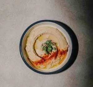 حمص تازه و لذیذ رستوران فرسکو، تزئین شده با روغن زیتون، پاپریکا و سبزی معطر. پیش‌غذای محبوب مدیترانه‌ای و خاورمیانه‌ای.