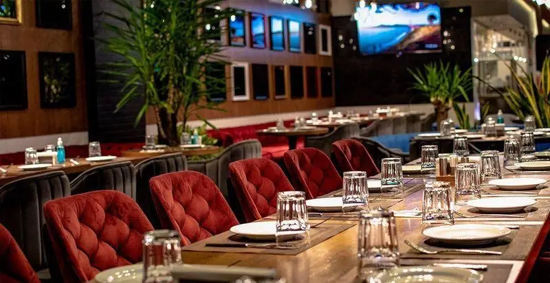 فضای داخلی لوکس رستوران ترکی تورکواز با میزهای چوبی آماده پذیرایی، صندلی‌های مخملی قرمز و دکوراسیون شیک و مدرن.