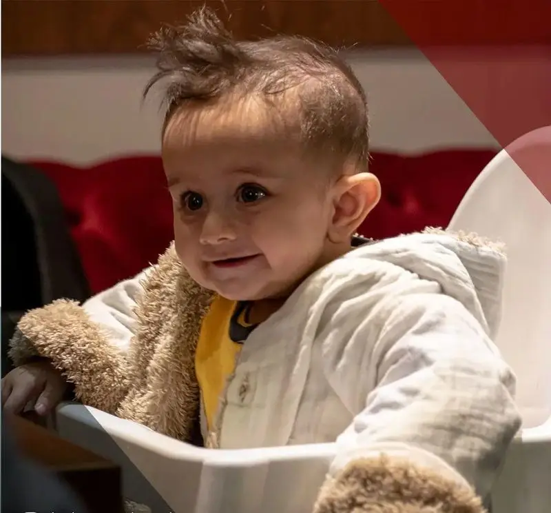 نوزادی دوست‌داشتنی با لبخندی شیرین و موهای سیخ در صندلی غذاخوری، نمادی از محیط گرم و خانوادگی رستوران ترکی تورکواز.