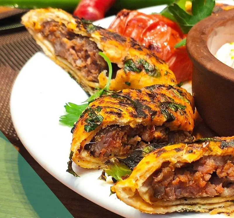 کباب بیتی لذیذ رستوران ترکی تورکواز، شامل رول‌های گوشت برشته شده در نان لواش با سبزیجات معطر، گوجه فرنگی کبابی و ماست.