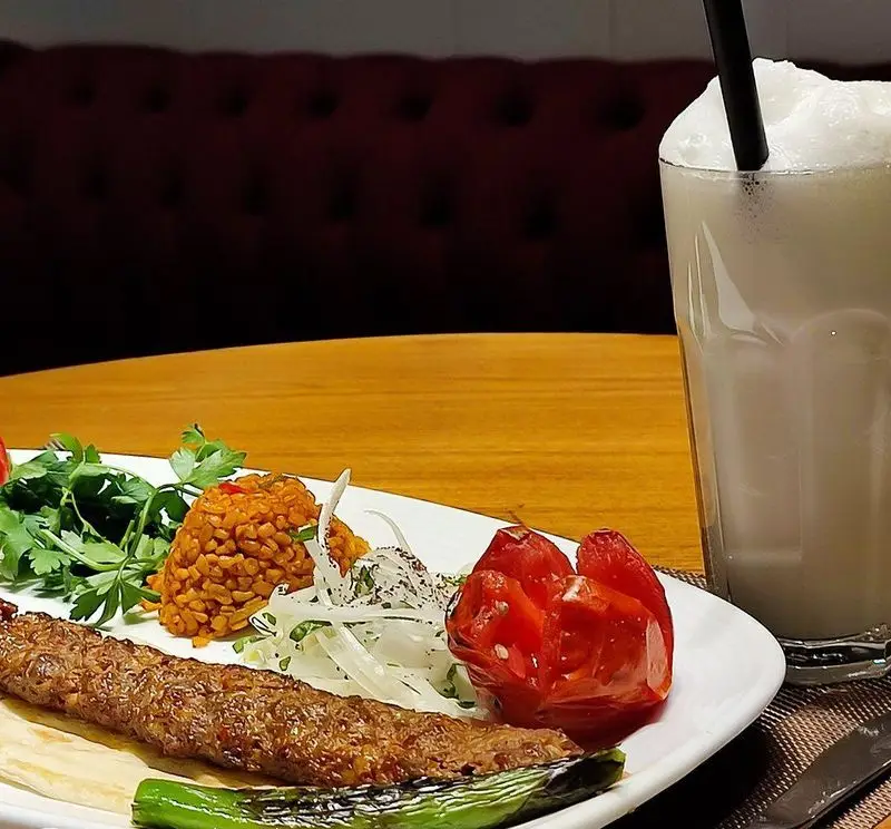 کباب آدانا، پلو بلغور، گوجه و فلفل کبابی در رستوران ترکی تورکواز. یک لیوان آیران خنک در کنار غذای اصیل ترکی.