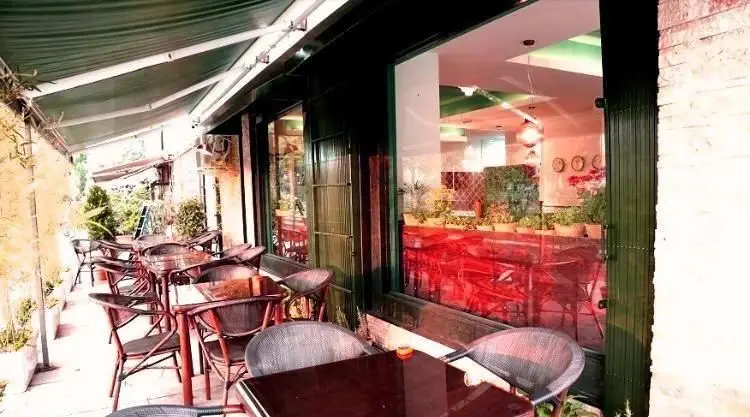 کافی شاپ ایل: فضای بیرونی جذاب با چیدمان میز و صندلی‌های شیک زیر سایبان سبز، ایده‌آل برای یک تجربه دلپذیر در کافه.