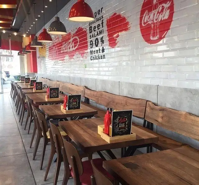 فضای داخلی تمیز و مدرن رستوران هایدا با میزهای چوبی و نیمکت، نورپردازی قرمز و دیوار کاشی‌کاری شده با طرح‌های 90% گوشت.