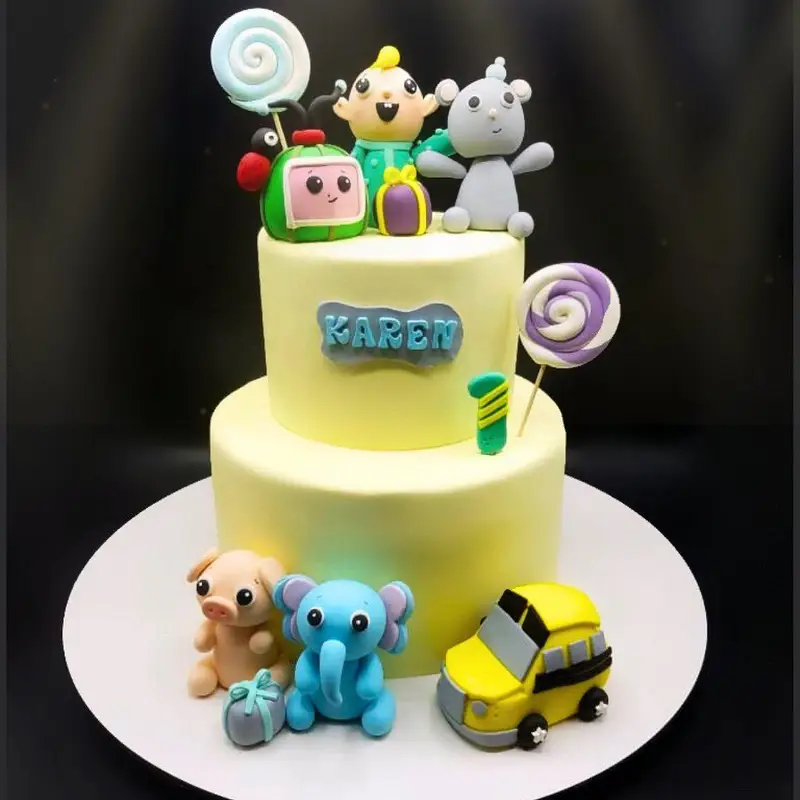کیک تولد دو طبقه زرد با تم محبوب کوکوملون و شخصیت‌های فوندانتی، مناسب جشن یک سالگی کودک از کافه قنادی کوک.
