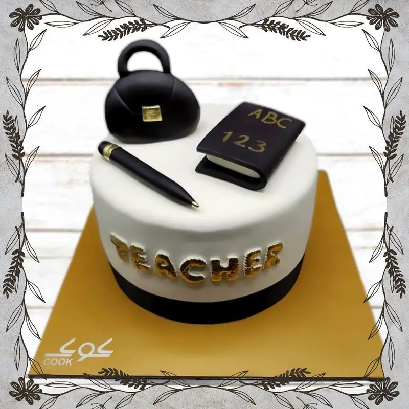 کیک سفید و مشکی روز معلم کافه قنادی کوک، با دکور طرح کیف، قلم و کتاب و نوشته طلایی "Teacher"، هدیه‌ای خاص برای استاد.