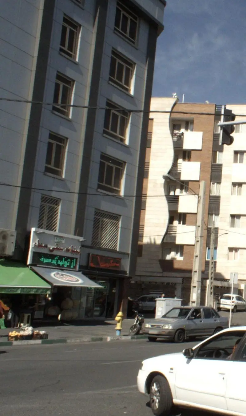 نمای بیرونی فروشگاه لبنیات سنتی سماء با تابلوی روشن، سایبان سبز، در یک روز آفتابی در خیابان شلوغ شهری با ماشین‌ها و عابران.