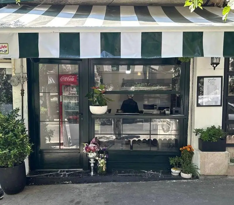 نمای بیرونی دنج و جذاب پیتزا گاردن، رستوران فست فود با سایبان سبز و سفید، دکوراسیون گل و گیاه و ورودی شیک.