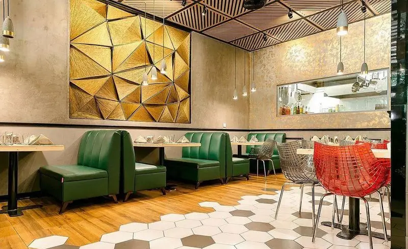 فضای داخلی مدرن و شیک رستوران پلاک با دیوار هنری طلایی، سقف چوبی، مبلمان سبز و آشپزخانه باز. محیطی جذاب برای مشتریان.