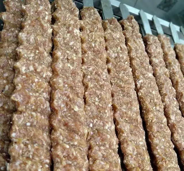 سیخ‌های ردیف شده کباب کوبیده خام و تازه، با آماده‌سازی ویژه و سنتی، آماده برای طبخ در کبابی منیریه. تجربه طعم اصیل.