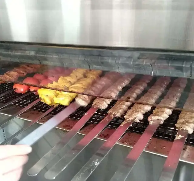 انواع کباب‌های تازه و لذیذ شامل کوبیده، جوجه و گوجه کبابی، در حال پخت بر روی منقل در کبابی منیریه. آماده سرو.