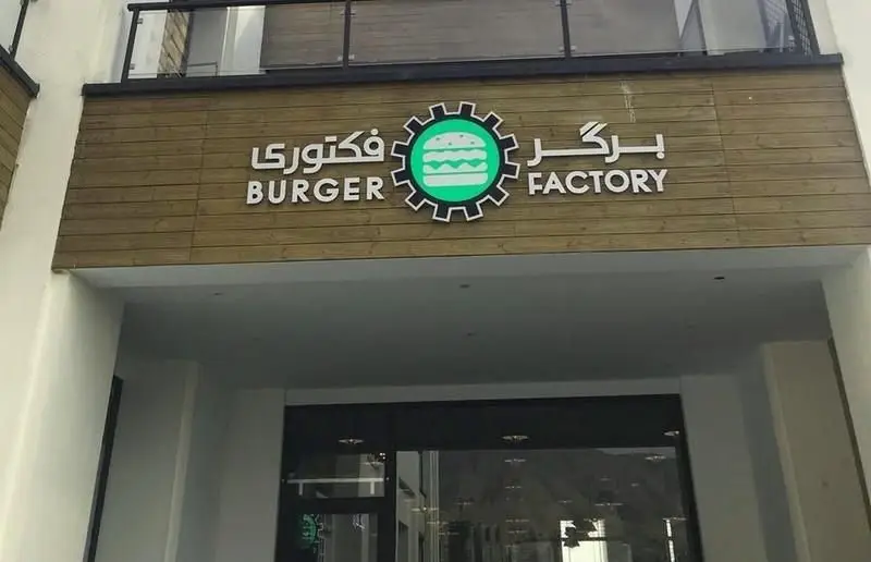 تابلوی مدرن رستوران برگر فکتوری (Burger Factory) با نام فارسی و انگلیسی، لوگوی خلاقانه همبرگر درون چرخ‌دنده، نمای بیرونی فست فود.